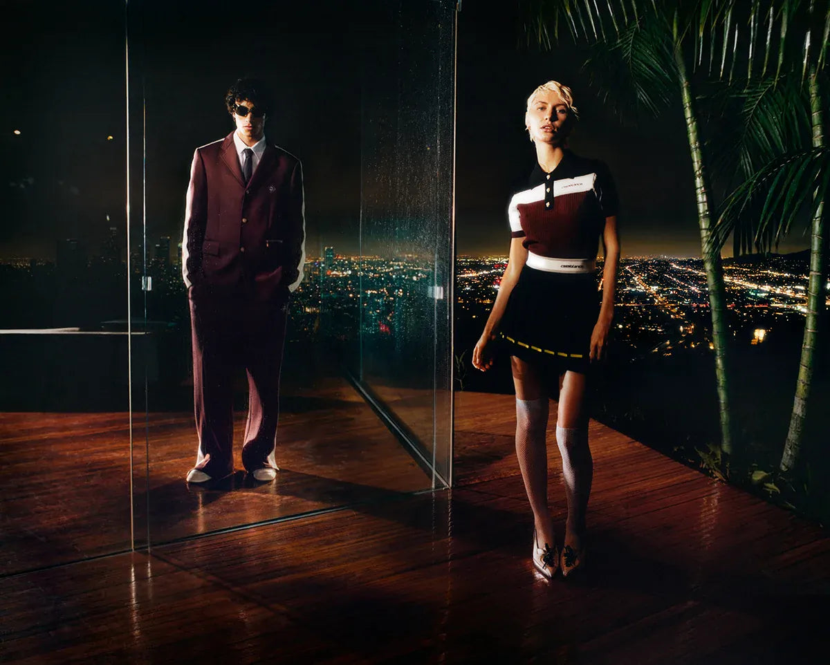 Casablanca SS26. Two people standing in a room with a large mirror reflecting a cityscape at night.