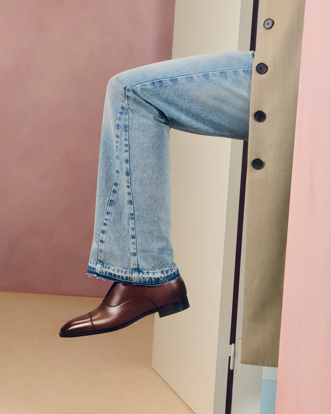Christian Louboutin SS26. Person wearing blue jeans and brown shoes against a pink and beige background