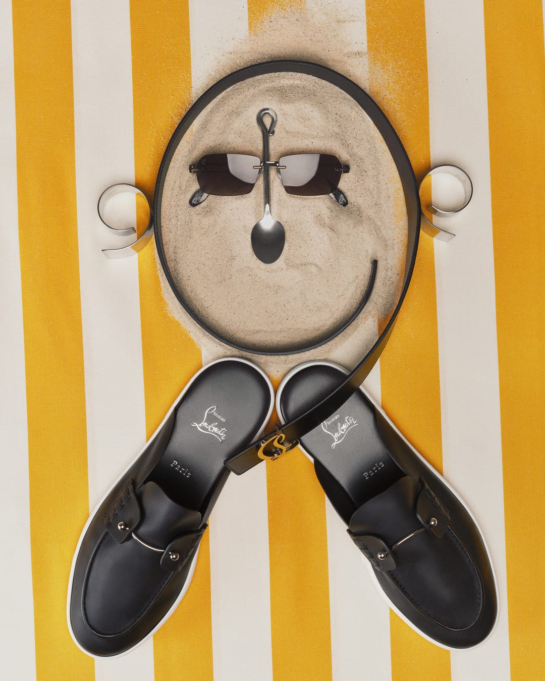 Christian Louboutin SS26. Black loafers with a face design on a yellow and white striped background