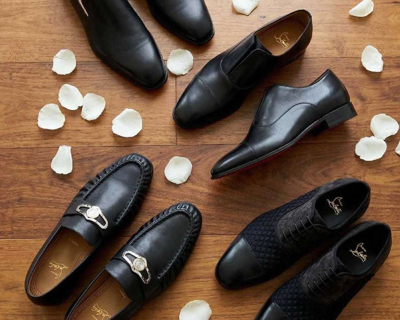 Christian Louboutin Black dress shoes on a wooden surface with scattered white petals