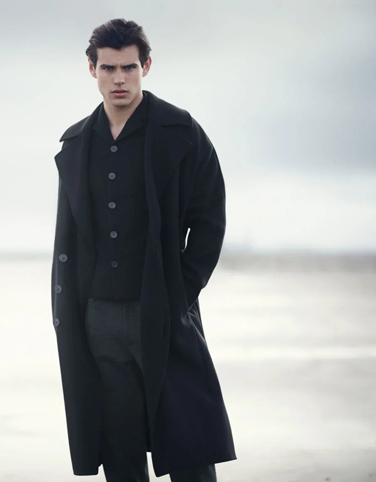 Emporio Armani clothing for men. Man wearing a long black coat against a neutral background
