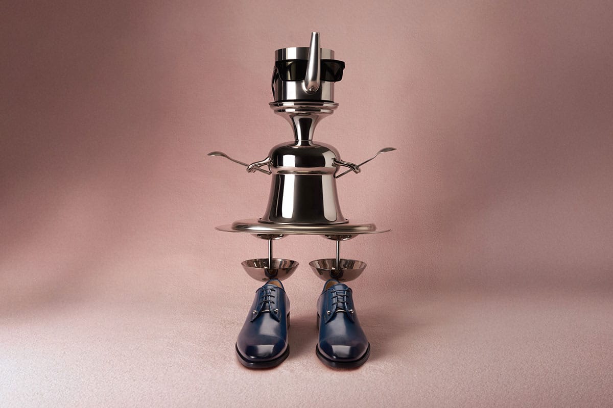 Christian Louboutin SS26. Still life metallic sculpture with pots and pans highlighting blue shoes, on a pink background