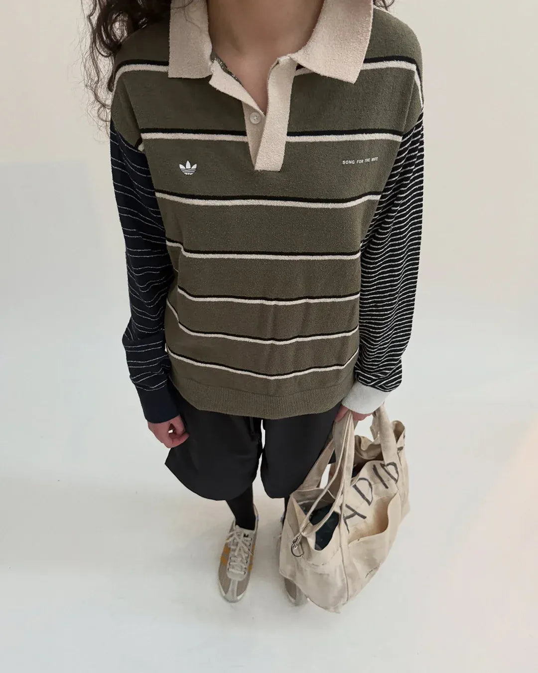 Song For The Mute x Adidas Originals SFTM007. Person wearing a striped shirt with an Adidas logo on a plain background