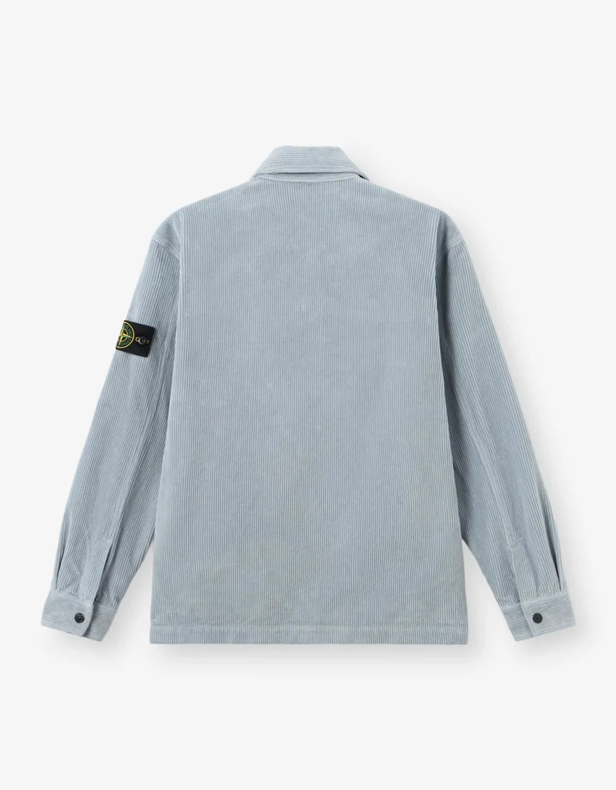 A light blue-gray Stone Island corduroy jacket shown from the back, featuring the signature black and yellow compass patch on the left sleeve, set against a clean off-white background.