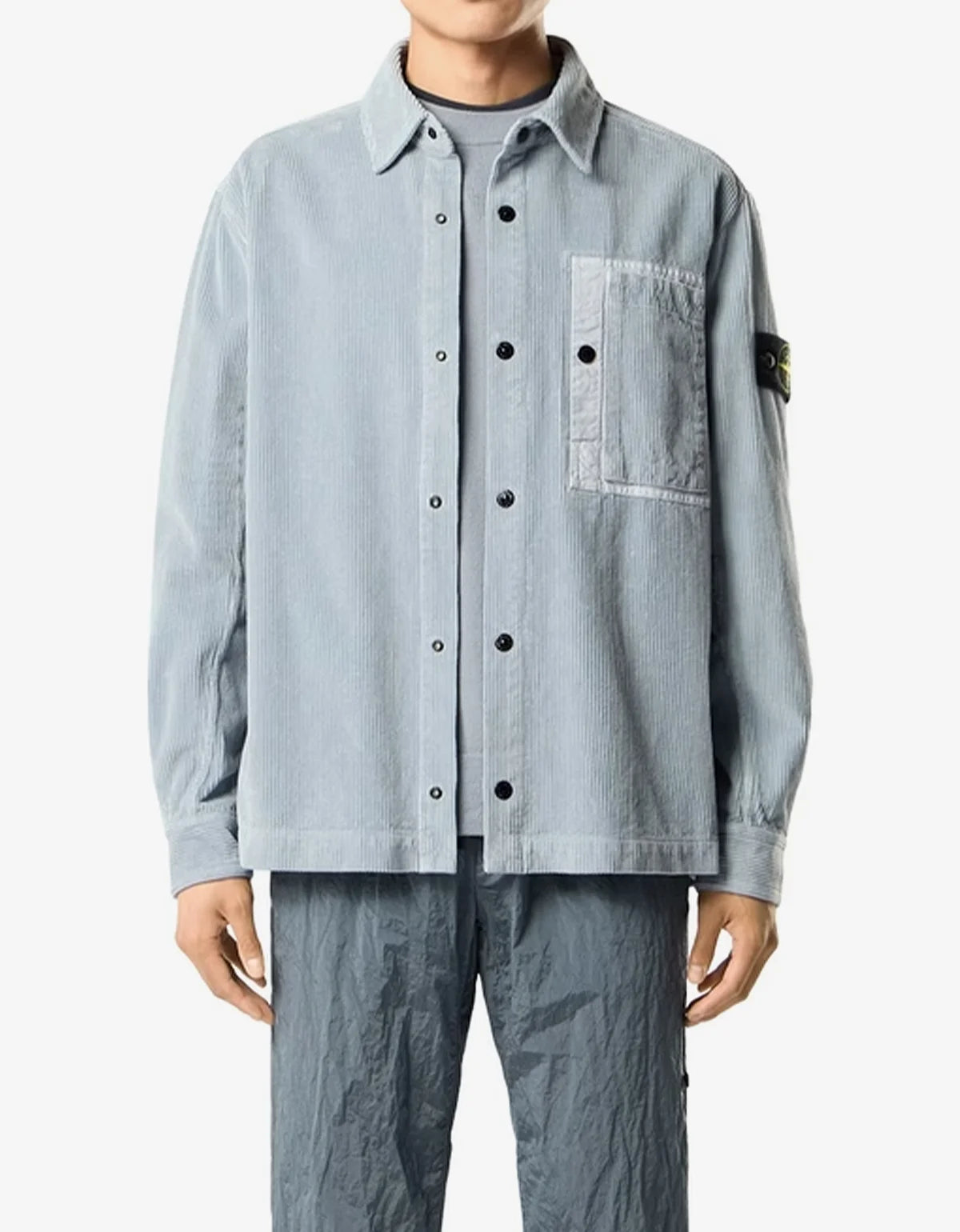 Close-up of a light blue corduroy button-up shirt with a pointed collar and black buttons, worn by a model.