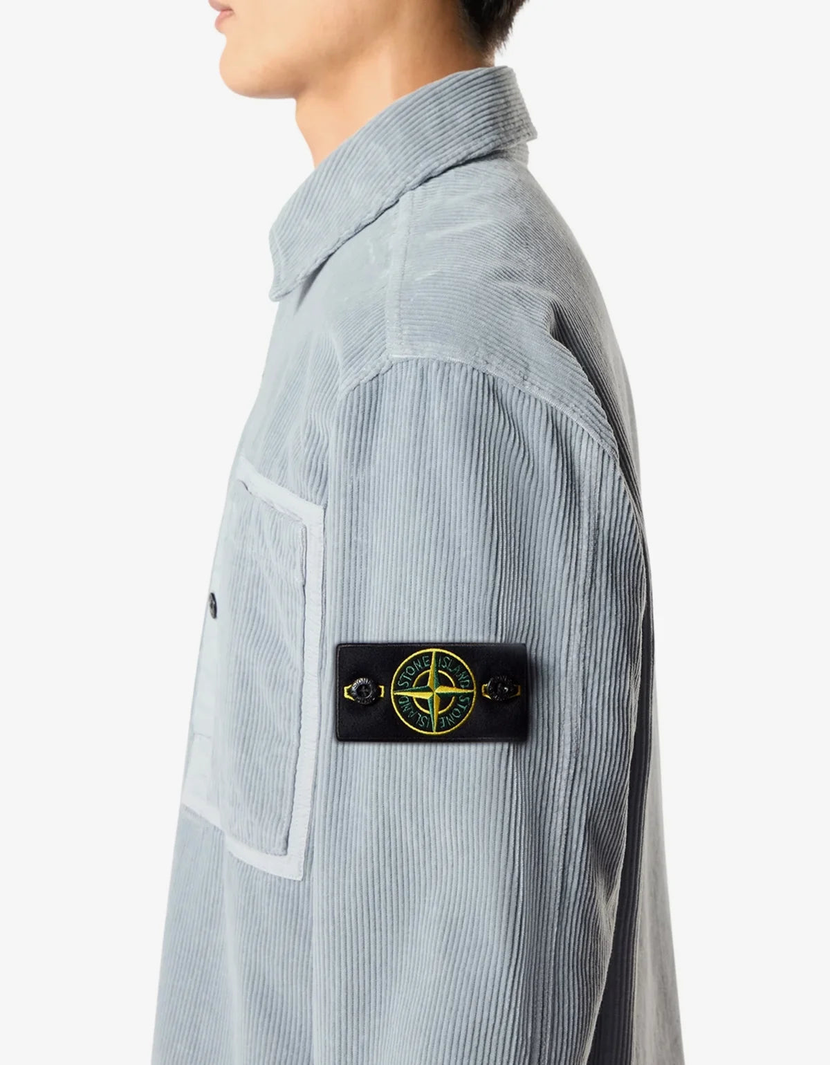 Close-up of a light blue corduroy button-up shirt with a pointed collar and black buttons, worn by a model. Side profile showing the Stone Island compass badge