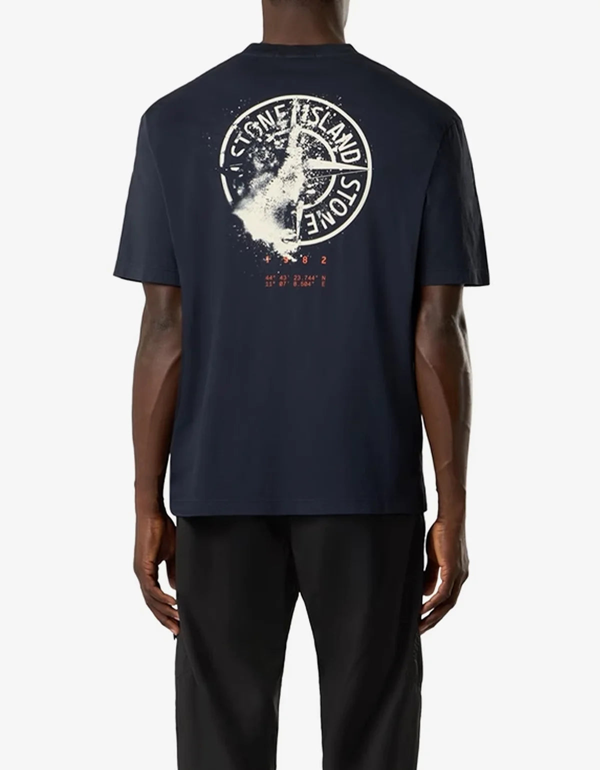 A man wearing a dark navy blue Stone Island t-shirt from the back, featuring a large white circular logo and cross graphic with red text on the upper back.