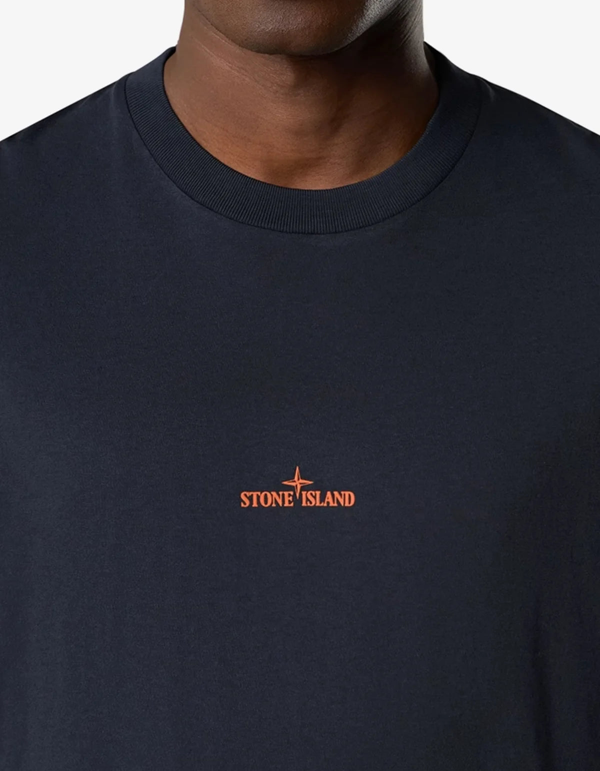 Close-up of a person wearing a dark navy crewneck t-shirt with a small orange Stone Island logo on the chest.