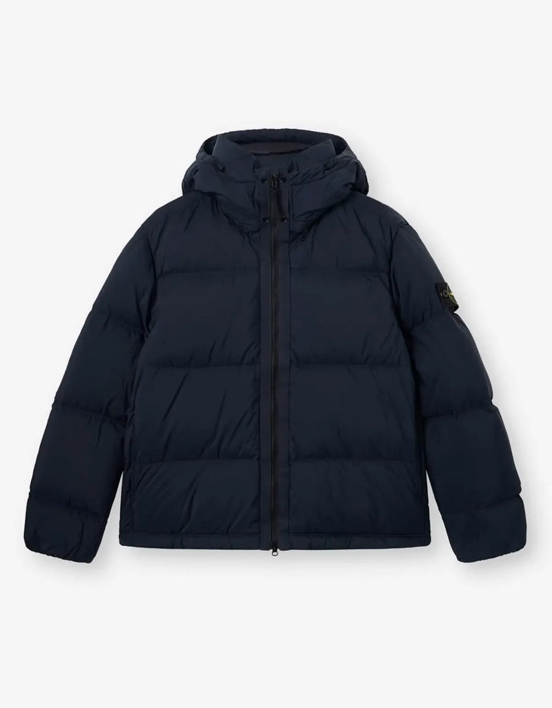 A dark navy blue hooded puffer jacket with horizontal quilting, a front zipper, and a small black brand patch on the left sleeve, displayed against a light gray background.