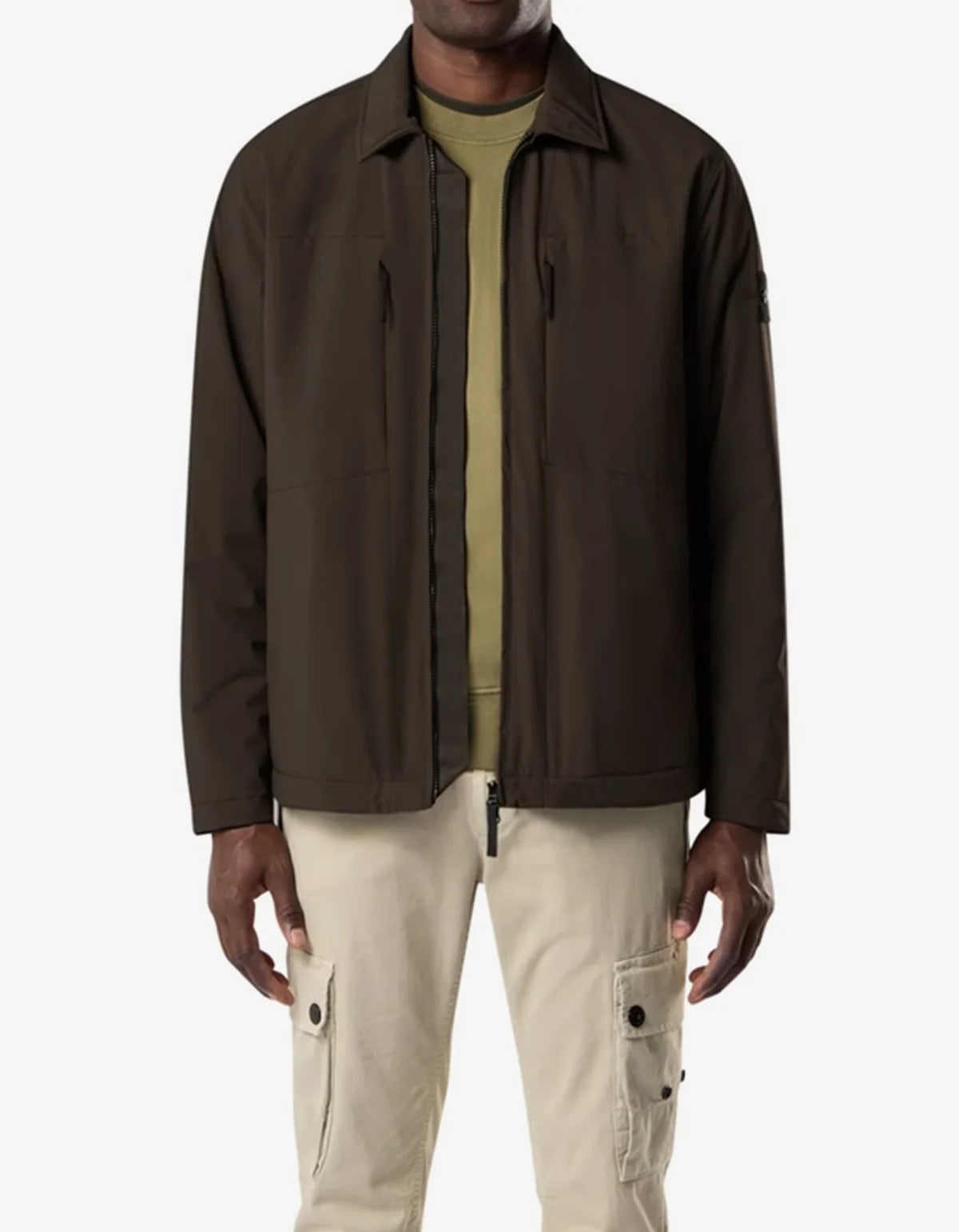 A man wearing a dark brown lightweight zip-up jacket over an olive green shirt and beige cargo pants, shown from the waist up against a light gray background.