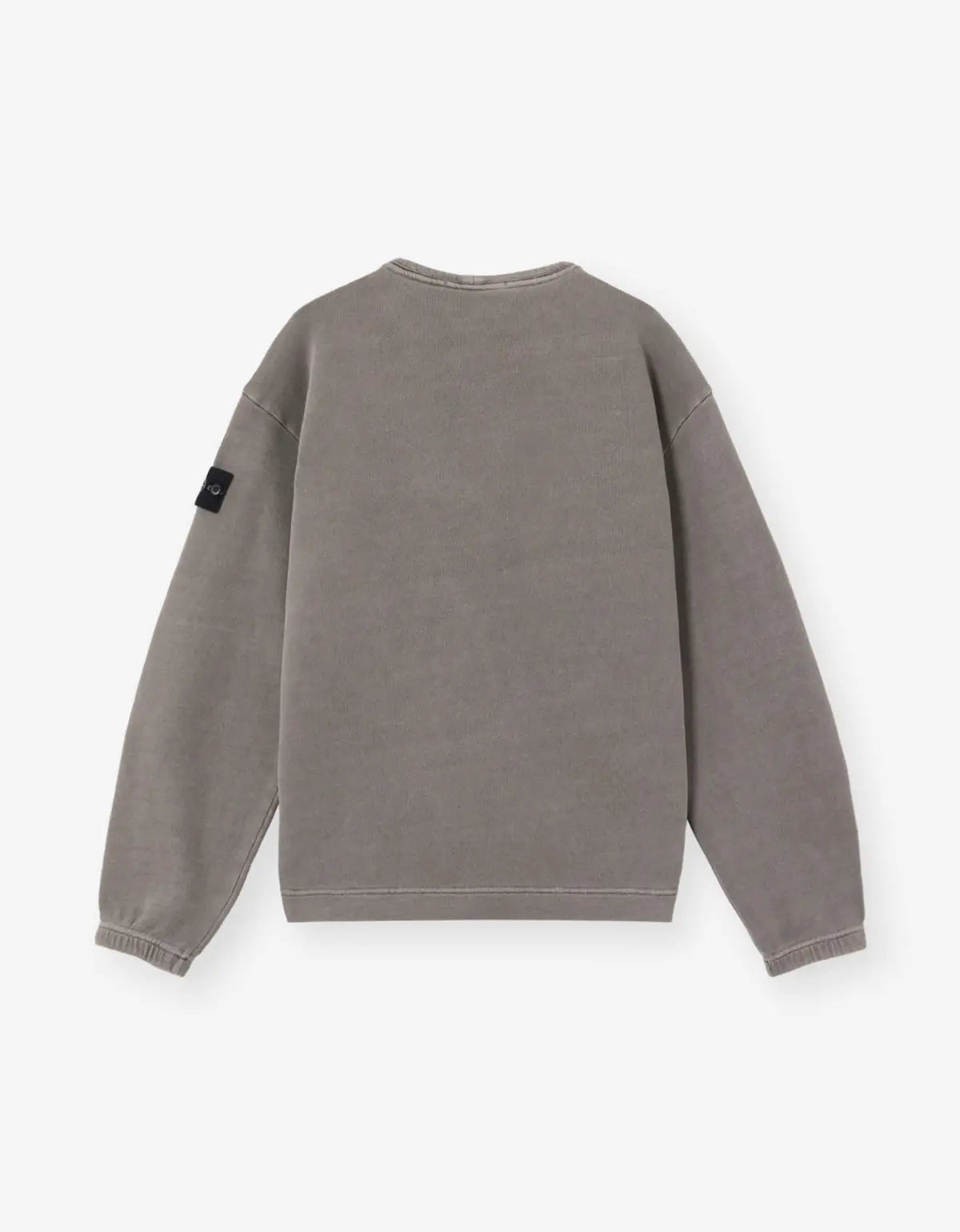A washed gray crewneck sweatshirt shown from the back, featuring a small black brand patch on the left sleeve, set against a plain light gray background.