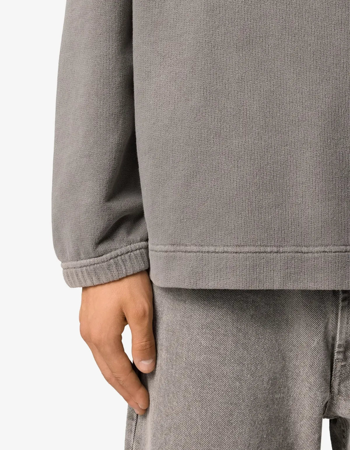 Close-up of a person wearing a heather gray long-sleeve top and matching gray pants, showing the sleeve cuff, hem, and hand against a plain light background.