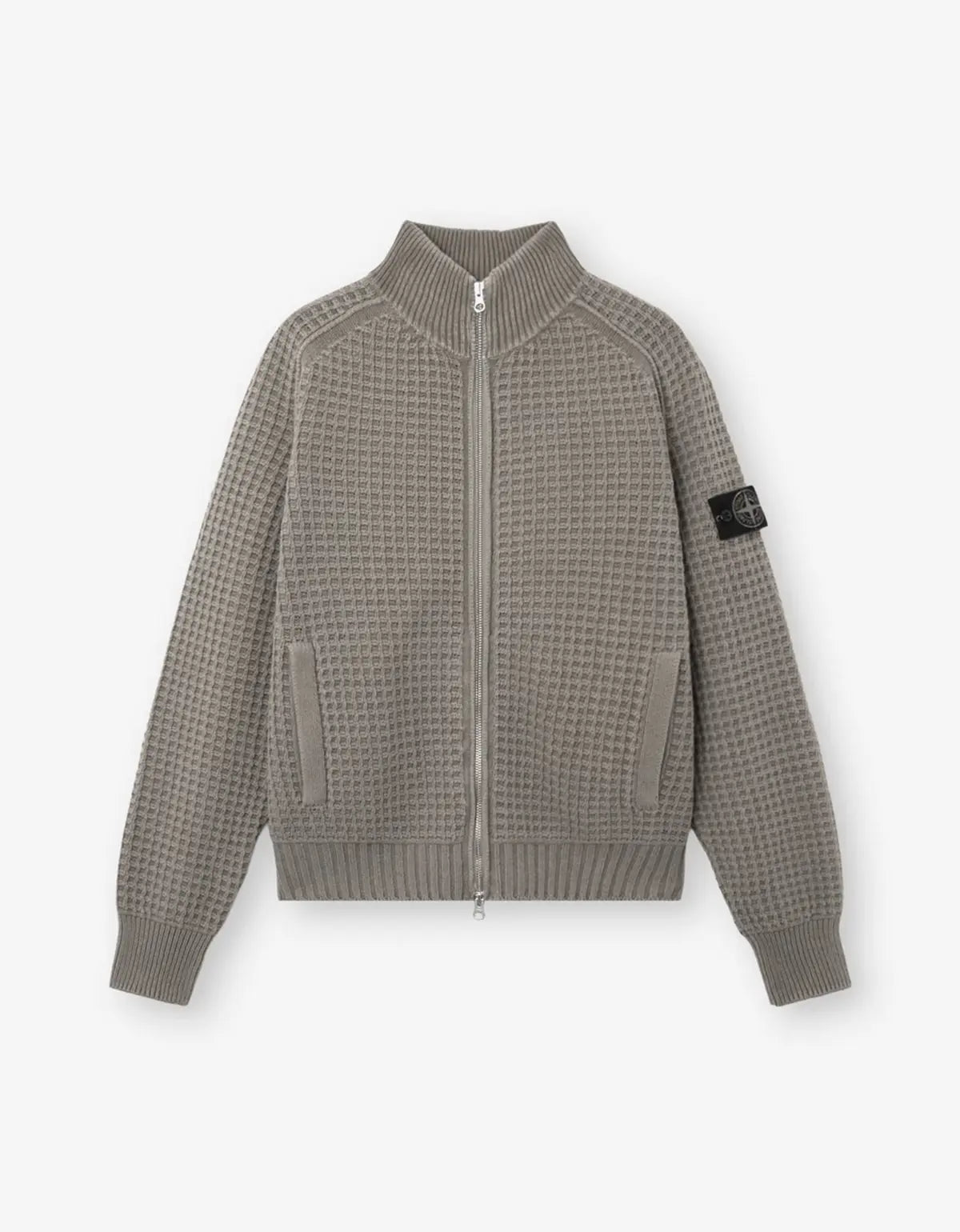 A waffle-knit zip-up jacket in a taupe-gray color, featuring a ribbed collar, cuffs, and hem, with a black Stone Island compass patch on the left sleeve, displayed against a light gray background.