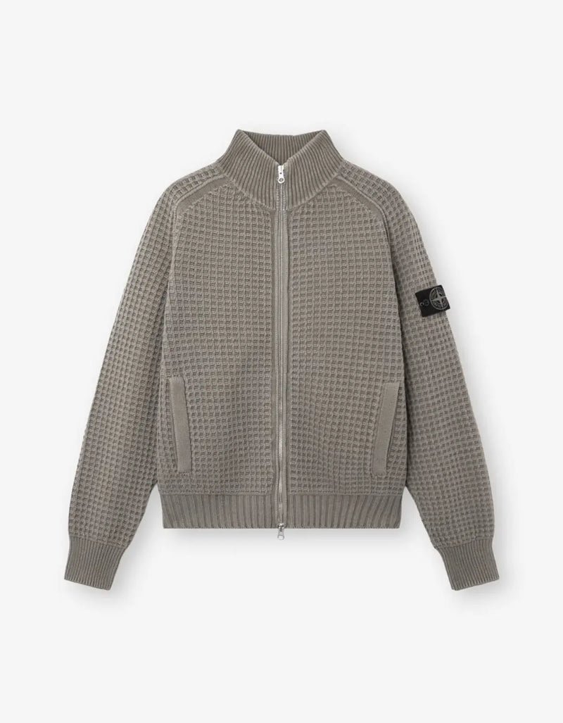 A waffle-knit zip-up jacket in a taupe-gray color, featuring a ribbed collar, cuffs, and hem, with a black Stone Island compass patch on the left sleeve, displayed against a light gray background.