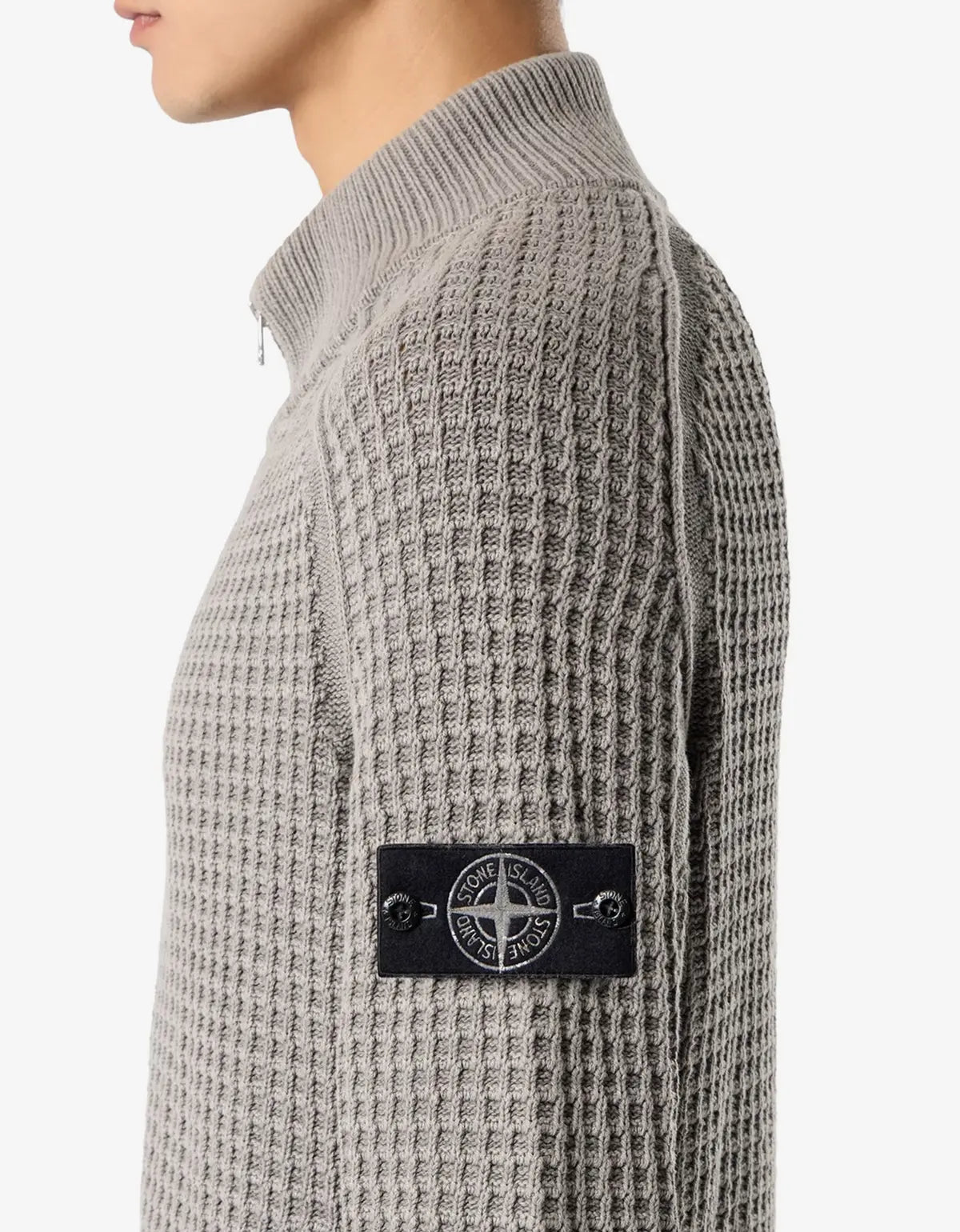 Close-up side view of a person wearing a gray waffle-knit mock-neck sweater with a black Stone Island logo patch on the upper arm.