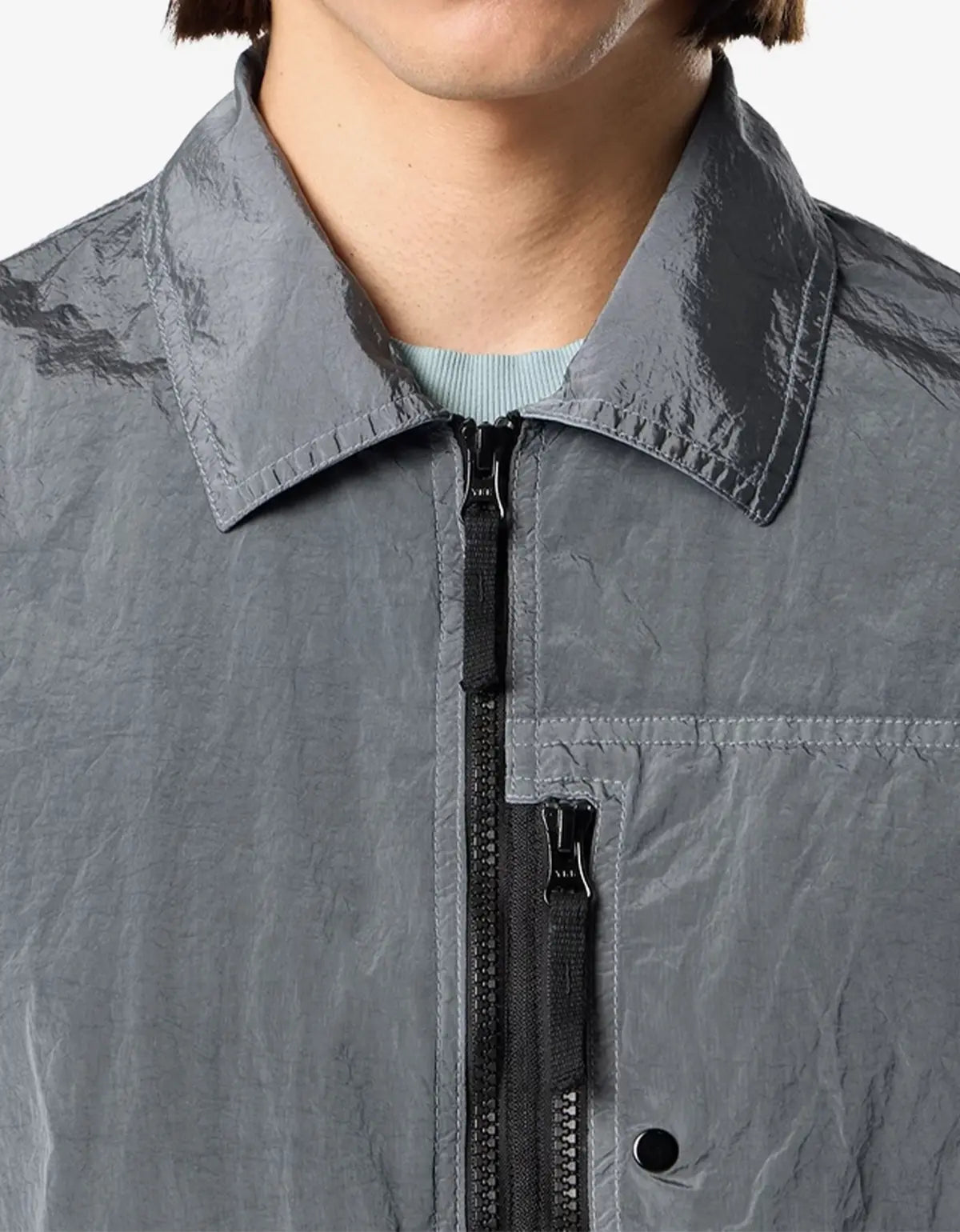 Close-up of a person wearing a gray crinkled lightweight jacket with a pointed collar, black front zipper, and a light blue ribbed undershirt visible at the neck.