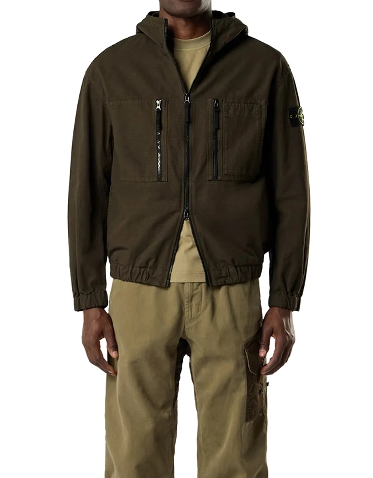 A model wearing a dark olive brown hooded zip-up jacket with multiple front pockets, paired with khaki pants and a beige t-shirt, shown against a plain white background.