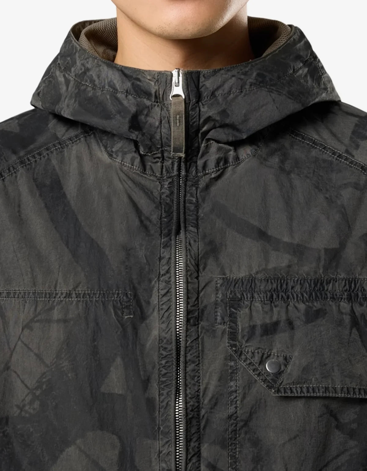 Close-up of a person wearing a dark gray hooded jacket with a subtle tonal camouflage pattern, featuring a front zipper and a chest pocket.