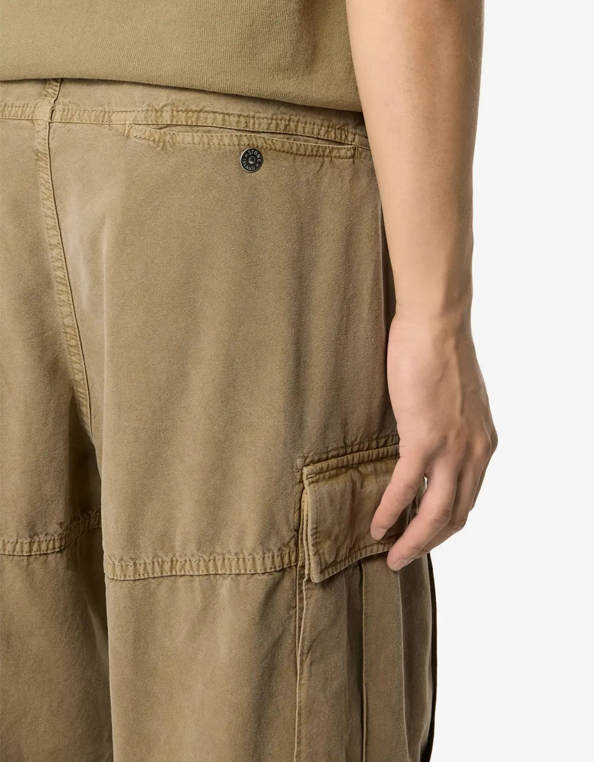 Close-up of a person wearing tan cargo pants, showing the back pocket and side cargo pocket with a hand resting near the pocket, against a plain light background.