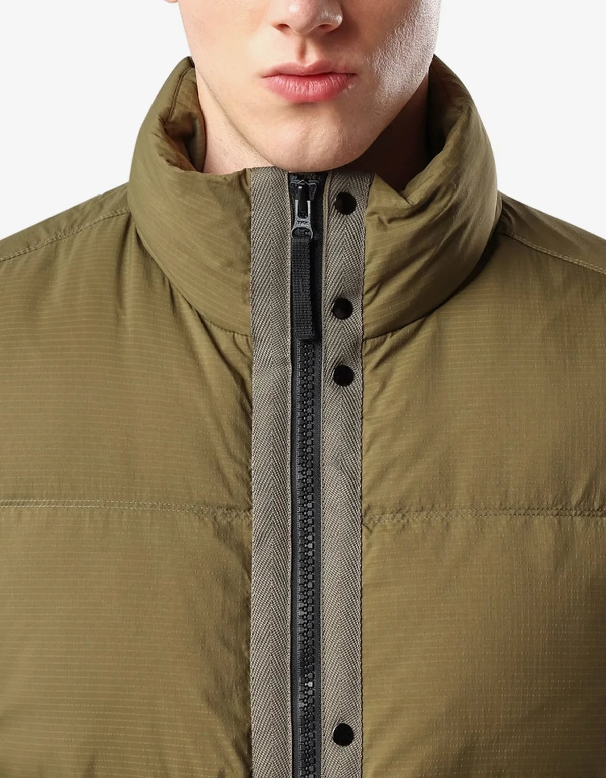 Close-up of a person wearing an olive green puffer jacket with a high collar, black zipper, and snap-button placket.