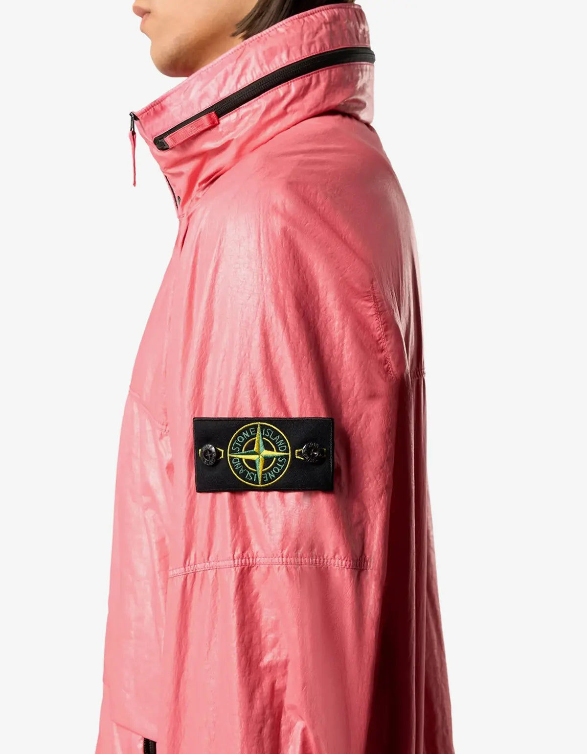 A close-up side view of a model wearing a pink waterproof jacket with a black Stone Island compass patch on the sleeve, set against a plain light gray background.