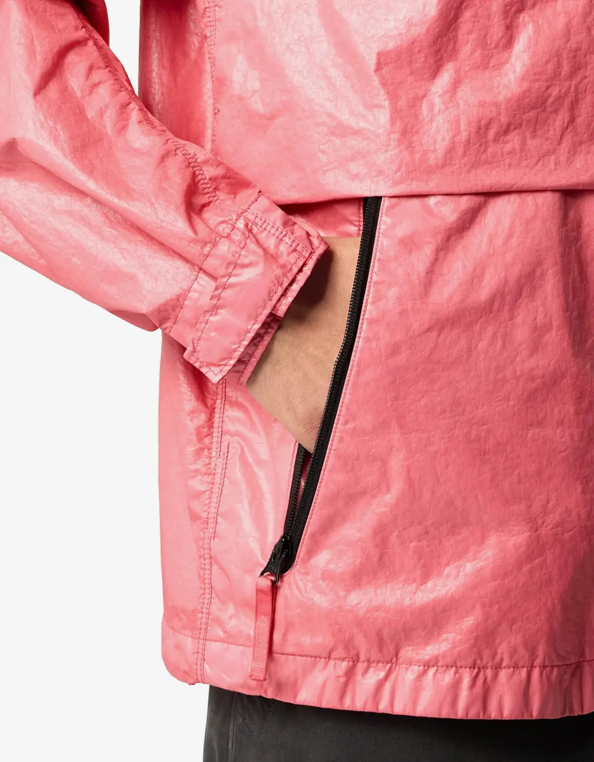 Close-up of a shiny pink lightweight jacket with a black zipper pocket and a hand tucked inside, shown against a plain light background.