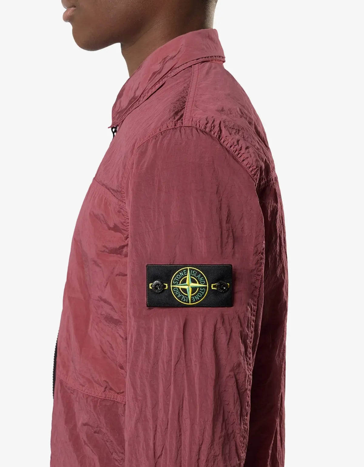 A close-up side view of a person wearing a dusty rose pink lightweight jacket, featuring the black Stone Island compass patch on the sleeve.