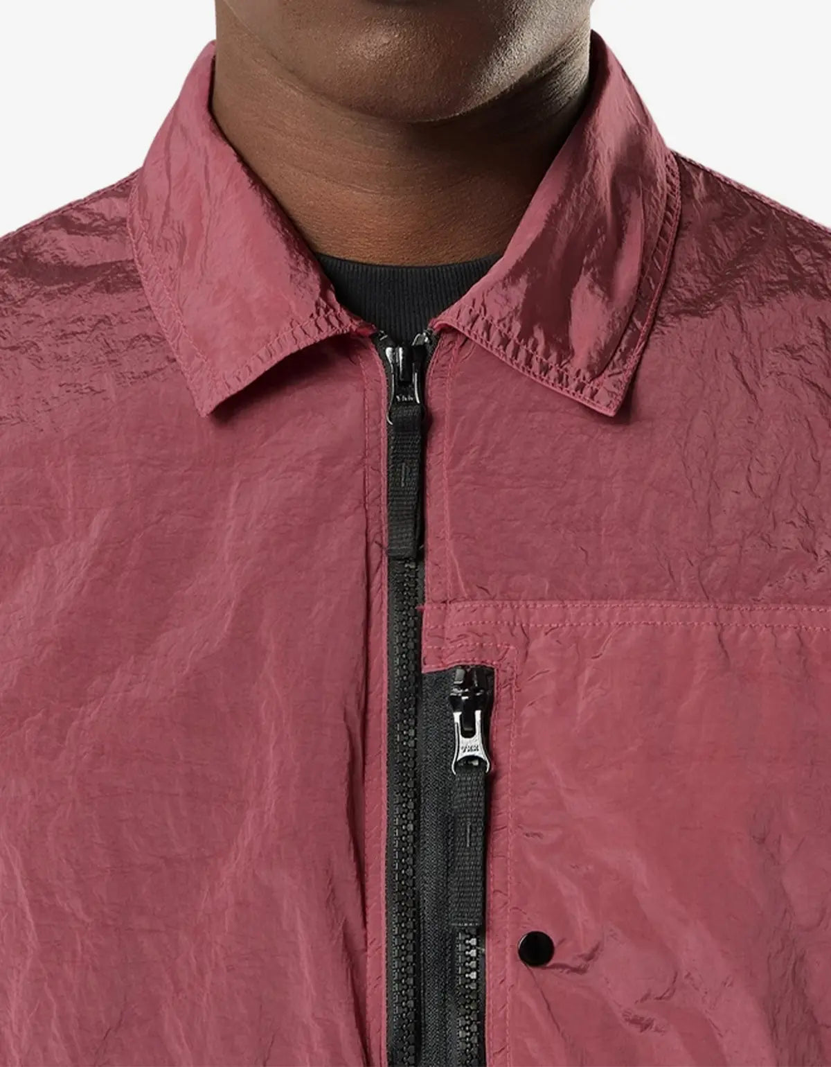 Close-up of a person wearing a crinkled dusty rose or mauve lightweight jacket with a black front zipper and a black inner shirt visible at the collar, against a plain light background.
