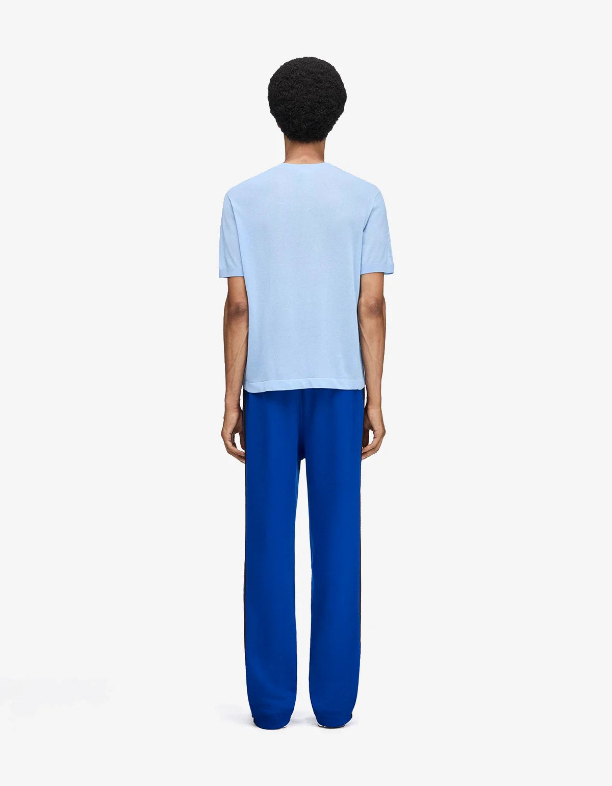 A model shown from the back wearing a light blue short-sleeve t-shirt and bright blue trousers, standing against a plain white studio background.