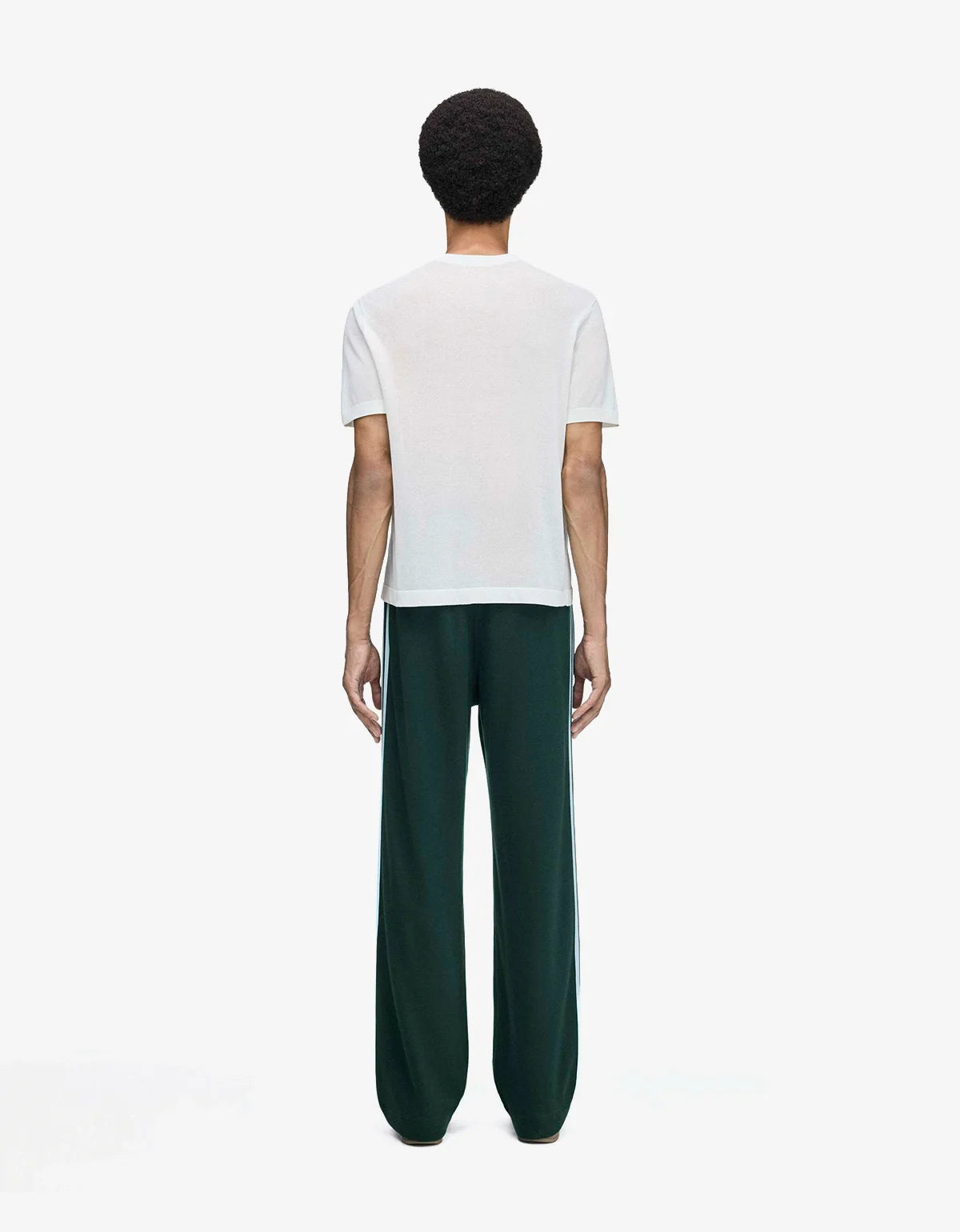 A model shown from the back wearing a white short-sleeve t-shirt and dark green wide-leg trousers with blue side stripes, set against a plain white studio background.