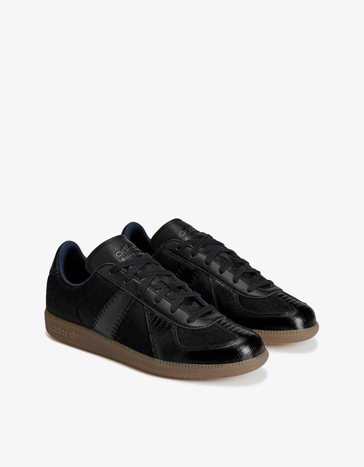 A pair of black low-top sneakers with glossy leather panels, black laces, and gum brown soles, displayed on a clean white background.