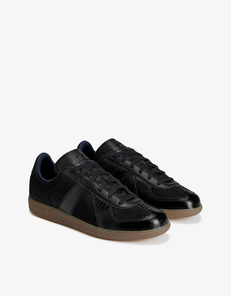 A pair of black low-top sneakers with glossy leather panels, black laces, and gum brown soles, displayed on a clean white background.