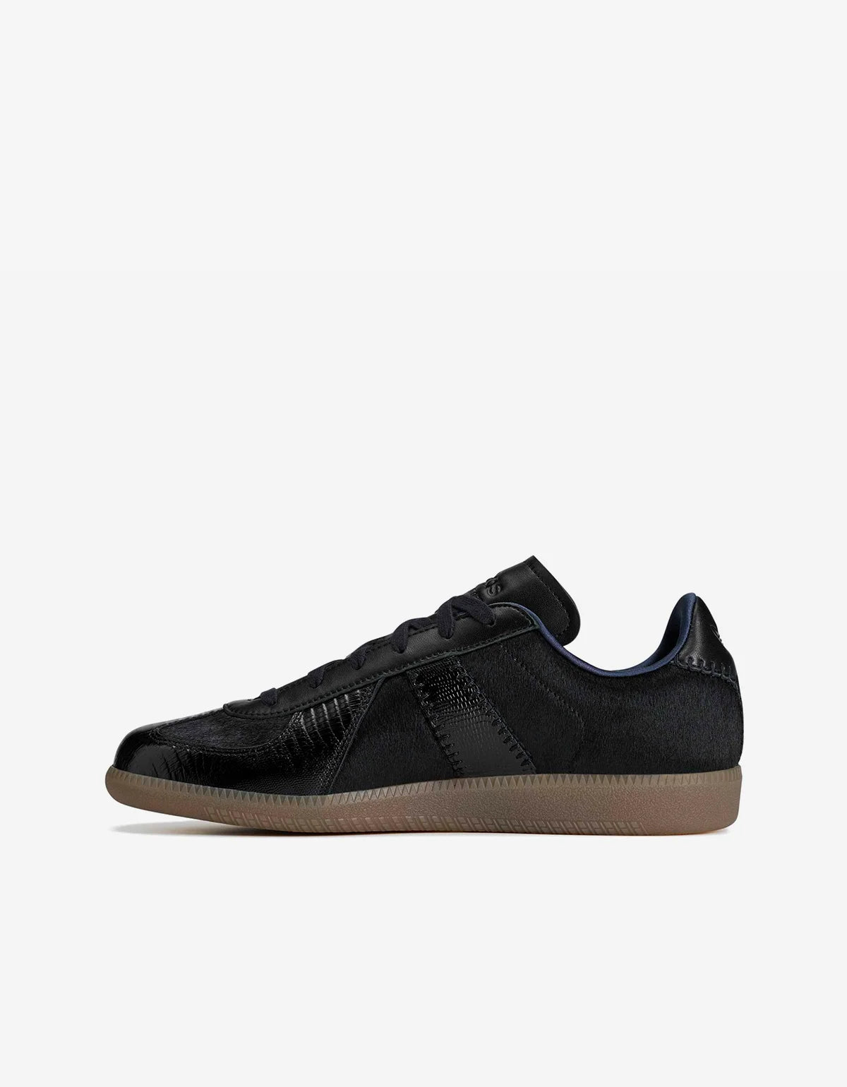 A black low-top sneaker with textured panels, black laces, and a gum brown sole, shown in profile against a light gray background.