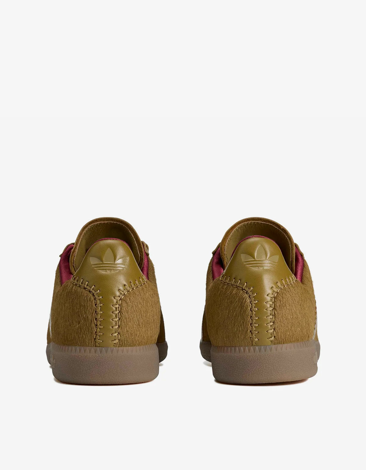A pair of Adidas low-top sneakers shown from the back, featuring a textured mustard yellow upper with a tonal embossed trefoil logo and a gum sole.