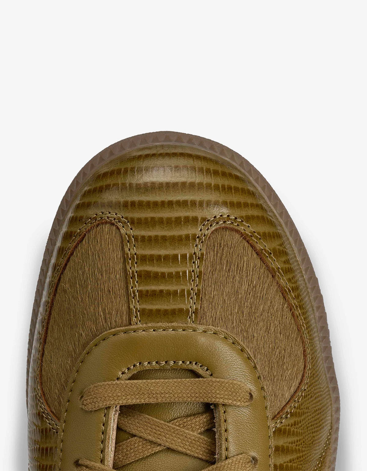 Close-up top view of a low-top sneaker in a warm tan/khaki color, showing textured crocodile-embossed panels, smooth leather overlays, and matching laces on a light gray background.