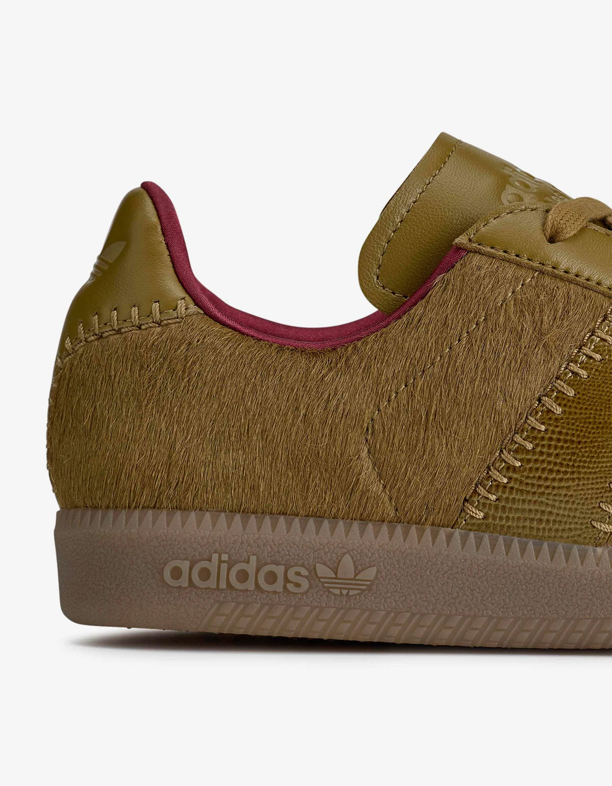 Close-up side view of an Adidas Wales Bonner sneaker featuring a textured olive green faux-hair upper, a brown suede-like midsole, and a burgundy inner lining, on a white background.