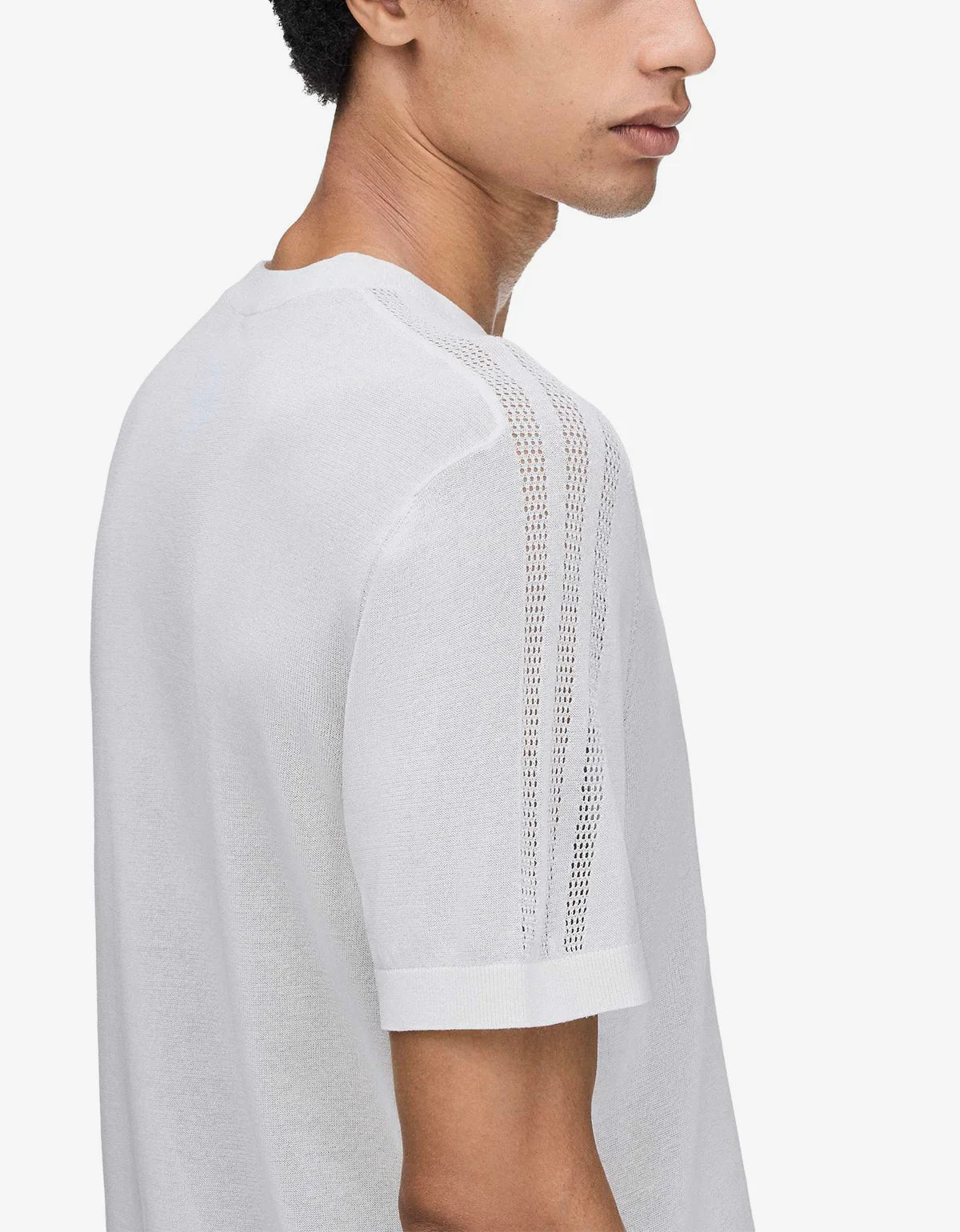 A close-up side profile of a man wearing a white short-sleeve knit t-shirt with a distinctive open-knit vertical stripe detail on the shoulder and upper sleeve.