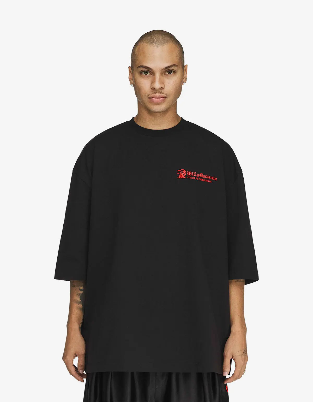 A man wearing a black oversized short-sleeve t-shirt with a small red 'Billy Reid' logo on the left chest, photographed against a light grey studio background.