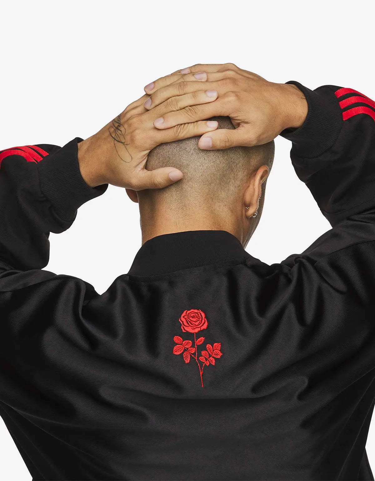 A man viewed from behind wearing a black jersey with red embroidered rose detail on the back and red stripes on the sleeves, set against a plain white background.