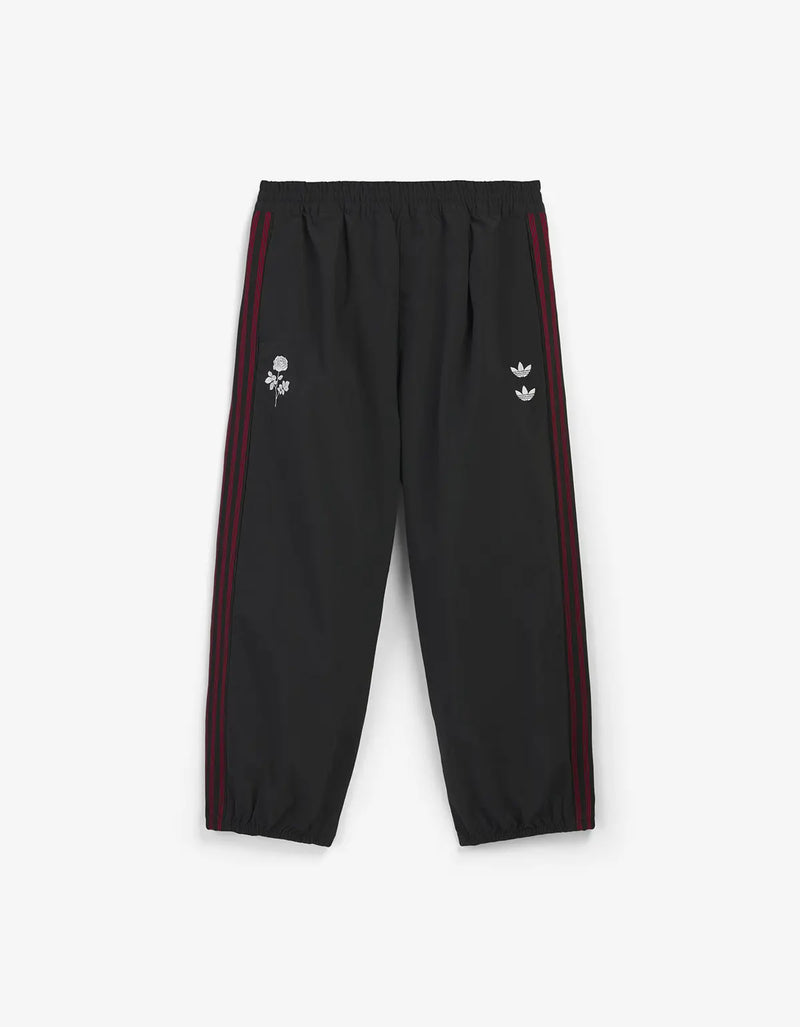 Black track pants with red side stripes and small white embroidered logos on the left thigh and right hip, shown flat against a light grey background.