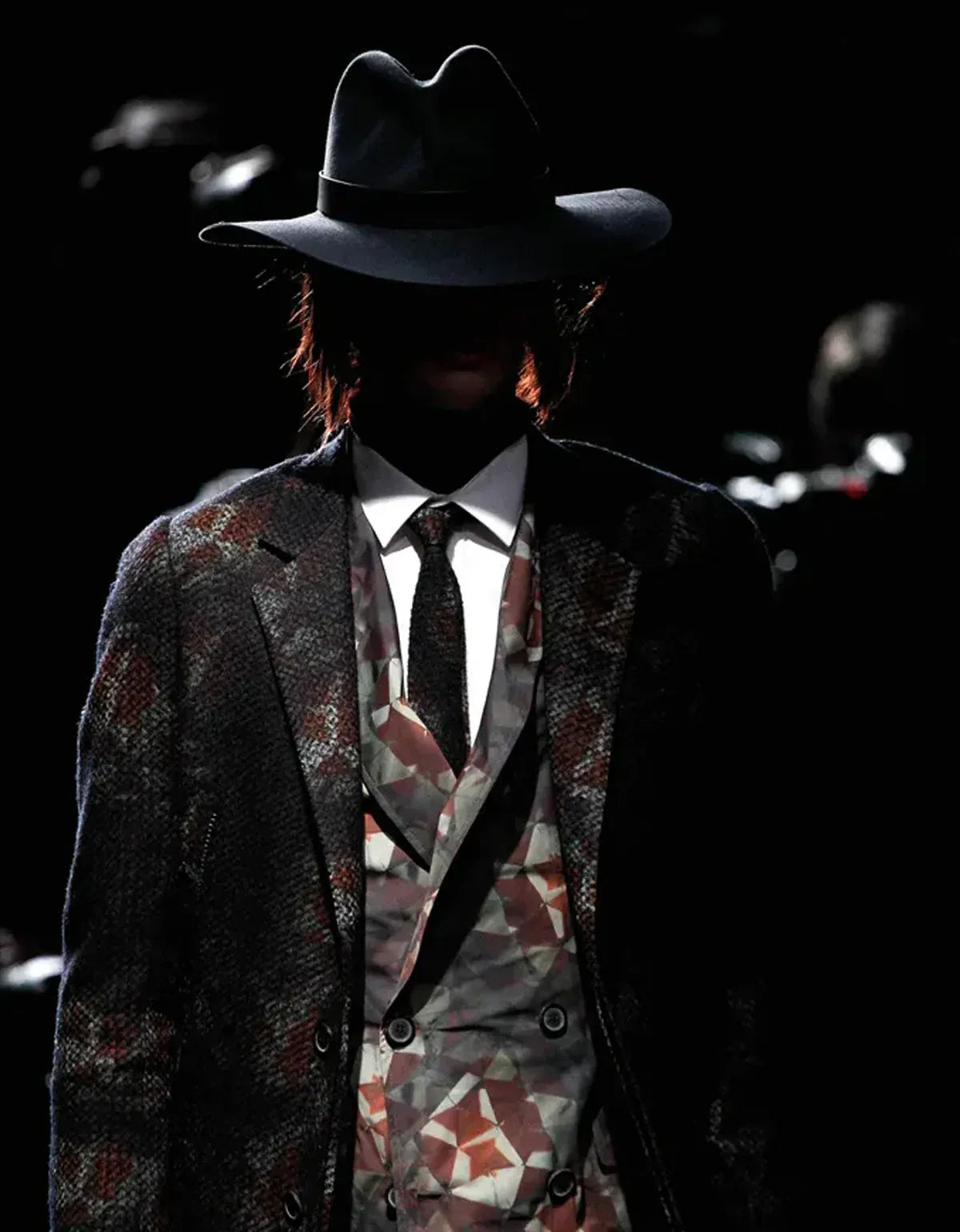 Lanvin clothing for men. Person wearing a patterned suit and wide-brimmed hat against a dark background